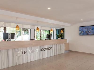 Bright hotel lobby with reception desk, three computers, and wall-mounted TV.