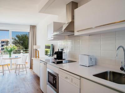 Modern bright kitchen with white furnishings and view of balcony and greenery.