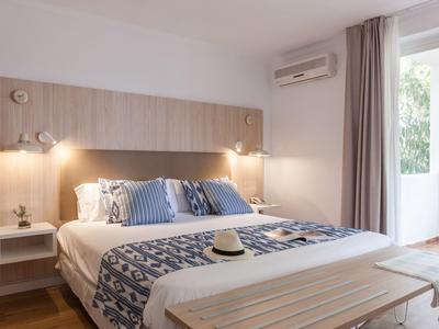 Bright hotel room with double bed, wooden accents, reading lamps, and balcony access.
