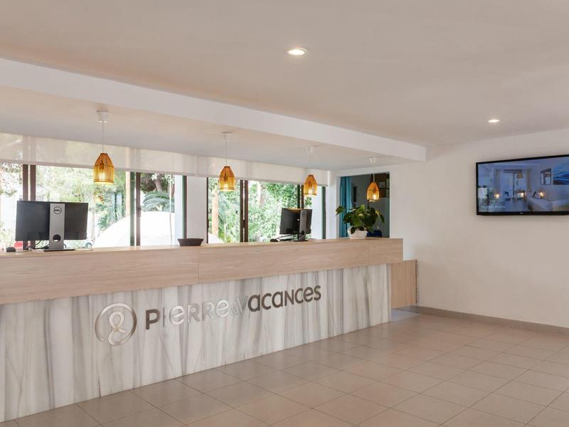 Modern hotel reception area with a long desk, hanging lights, and a wall-mounted screen.