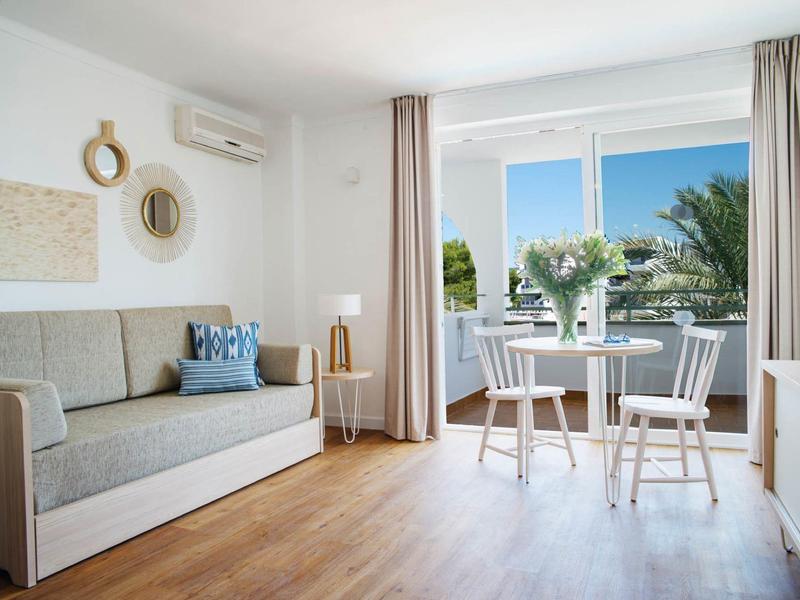 Bright modern living room with sofa, glass door opening to balcony overlooking sea.