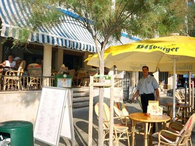 Zona exterior de una cafetería con mesas, sillas y sombrillas en un día soleado
