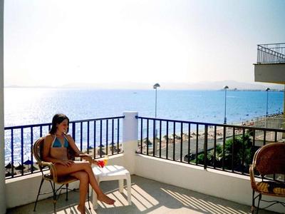 Persona sentada en silla de balcón con vista al mar y cielo soleado de fondo.
