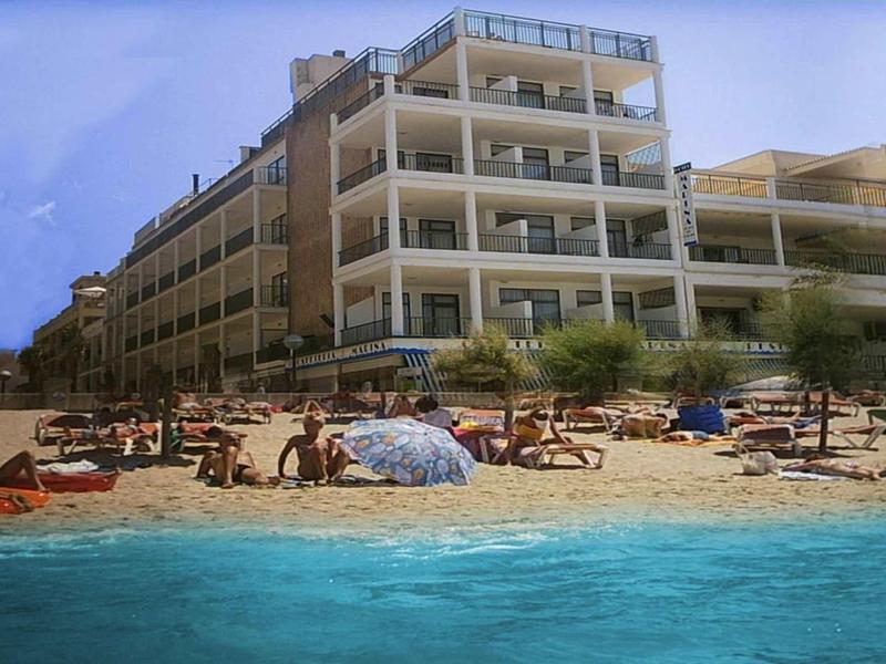 Mehrstöckiges Hotel am Strand mit vielen Sonnenschirmen und blauen Meer im Vordergrund.
