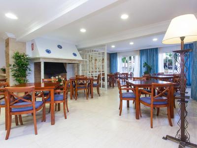 Restaurant lumineux avec chaises en bois, tables, cheminée et lampe sur pied dans un hôtel.