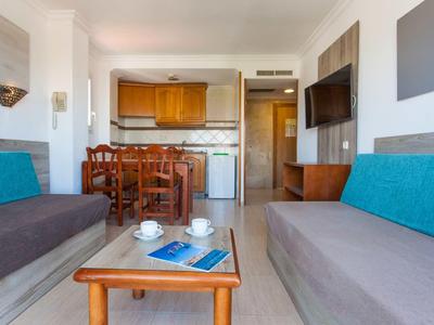 Wohnzimmer mit zwei grauen Sofas, Holztisch, Fernseher an der Wand und Essbereich mit Holzstühlen.