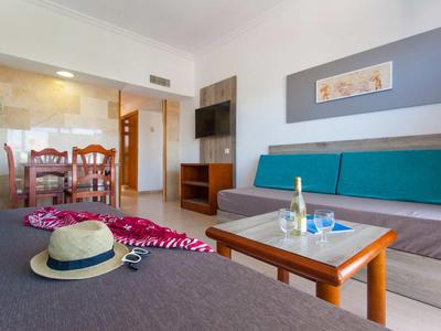 Salon lumineux avec canapés, table, télévision et vue sur la salle à manger dans une location de vacances.