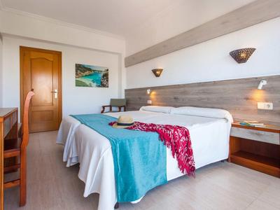 Helles Hotelzimmer mit zwei Einzelbetten, Holzmöbeln und bunter Bettdecke auf weißer Bettwäsche.