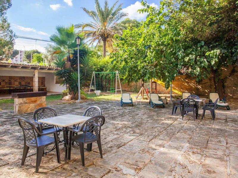 Großer Garten mit gepflastertem Boden, mehreren Sitzgruppen, Bäumen und einer Kinderschaukel.