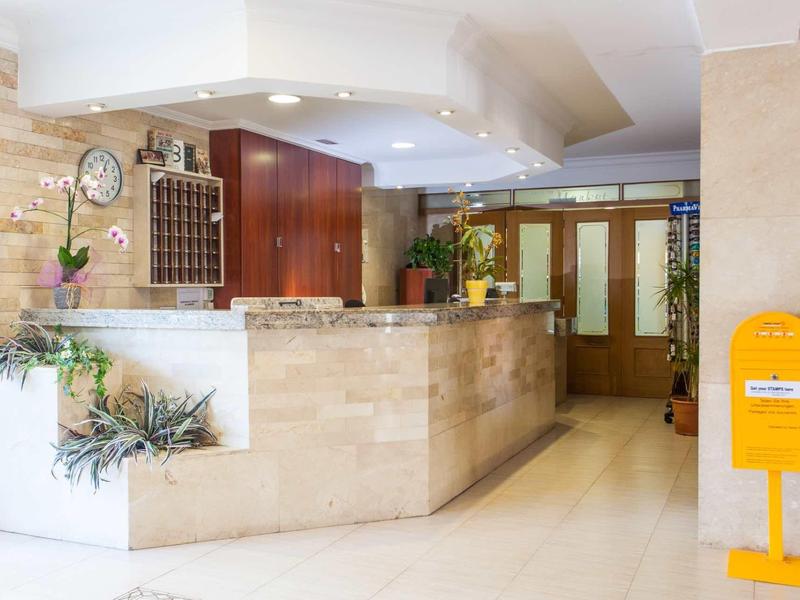 Heller Empfangsbereich mit Steintheke, Holzmöbeln, Pflanzen und gelbem Briefkasten in modernem Design.