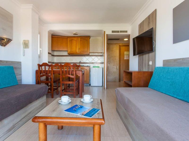 Wohnzimmer mit zwei grauen Sofas, Holztisch, Fernseher an der Wand und Essbereich mit Holzstühlen.