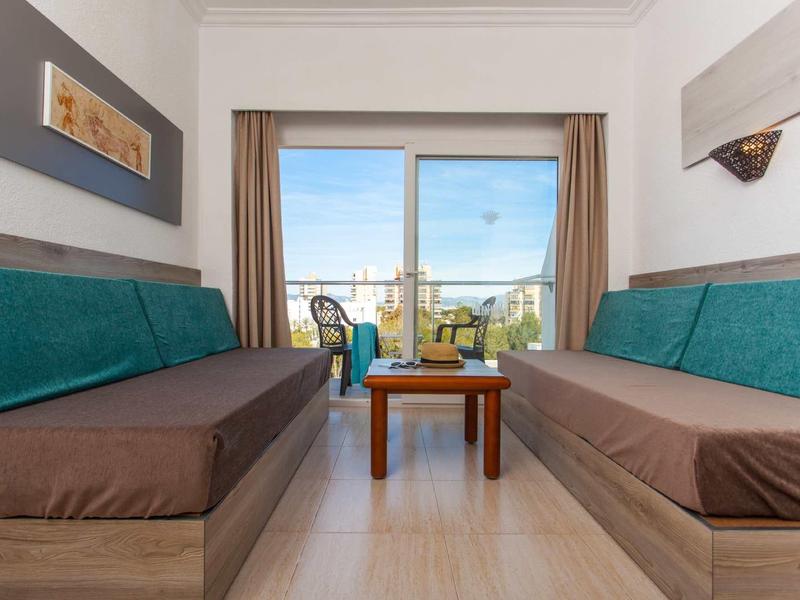 Wohnzimmer mit zwei langen Sofas, Kleinem Holztisch und großer Glas-Schiebetür zum Balkon.