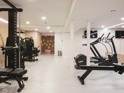 Moderner Fitnessraum mit Kraft- und Cardiogeräten auf hellgraßem Boden und weißen Wänden.