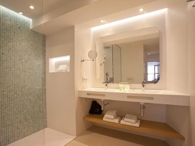 Moderne badkamer met lichte tegels, grote spiegel en extra handdoekenrek onder de wasbak.