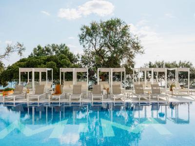 Groot helder zwembad met witte parasols en ligstoelen in een rustige hotelomgeving.