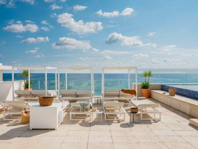 Moderne dakterras met wit meubilair, planten en uitzicht op zee onder een blauwe hemel.