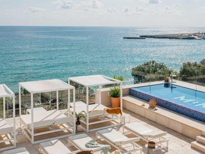 Moderne hotelterras met ligstoelen en zwembad, uitzicht op rustige blauwe zee bij heldere lucht.