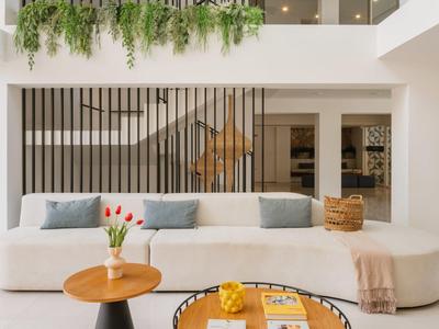 Lichte moderne woonkamer met gebogen bank, houten tafels en groene planten aan het plafond.