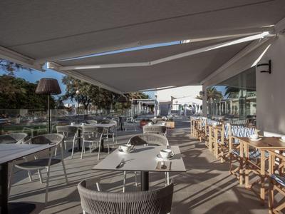 Modern hotelrestaurant met witte tafels en stoelen onder een zonnescherm.