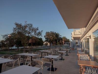 Terras met witte tafels en stoelen voor een hotel, bomen en heldere avondstemming.