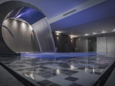 Modern binnenzwembad met waterval en stijlvolle verlichting in een hotel.