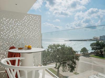Licht balkon met uitzicht op water, wit hek en kleine ronde tafel met stoelen.