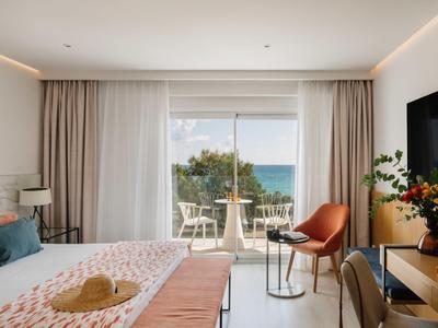 Lichte hotelkamer met tweepersoonsbed, balkon met zeezicht en moderne inrichting.