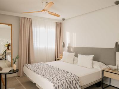 Moderne hotelkamer met groot bed, witte muren en natuurlijke gordijnen.
