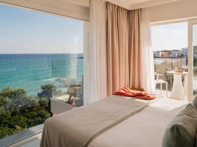 Hotelkamer met groot raam en uitzicht op zee, toegang tot balkon met uitzicht op de kust.