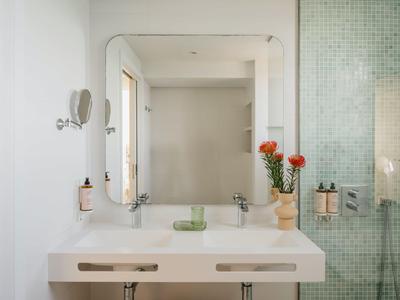 Heldere badkamer met grote spiegel, witte wastafel en glazen douche met mozaïektegels.