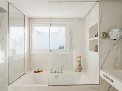 Moderne badkamer met wit bad, grote ramen en glazen douchewand.