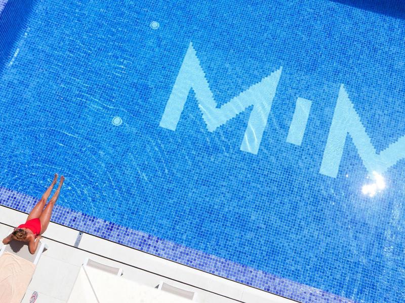 Kobieta odpoczywa na brzegu jasnoniebieskiego basenu z napisem MIM.