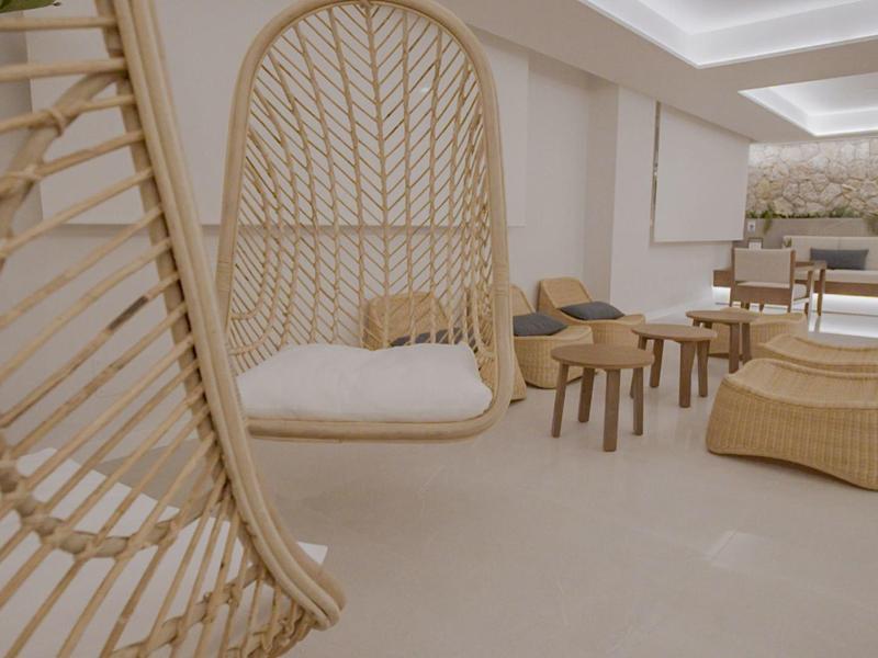 Jasna przestrzeń wypoczynkowa z krzesłami rattanowymi, wiszącym łóżkiem i widokiem na taras z meblami lounge.