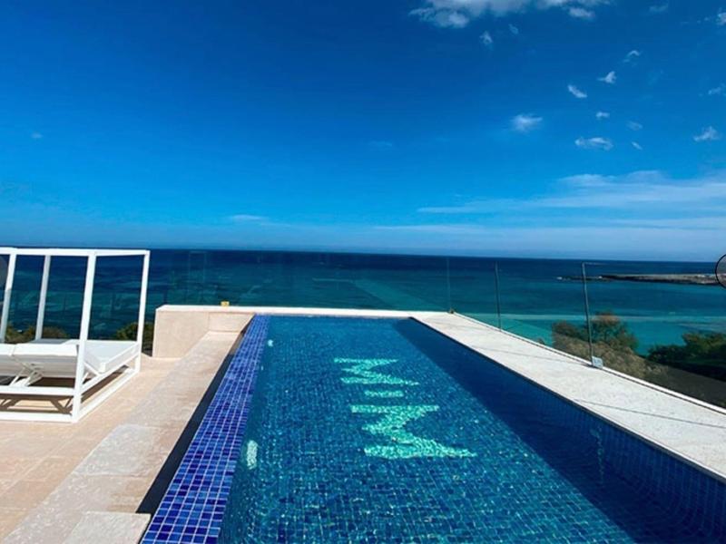 Basen typu infinity z przejrzystą niebieską wodą i widokiem na morze pod błękitnym niebem.