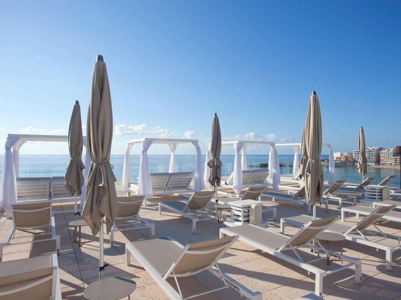 Taras słoneczny z leżakami i zamkniętymi parasolami z widokiem na morze pod czystym niebem.