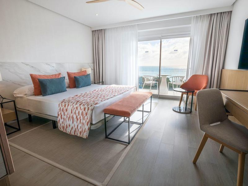 Nowoczesny pokój hotelowy z łóżkiem podwójnym, częścią wypoczynkową i tarasem z widokiem na morze.