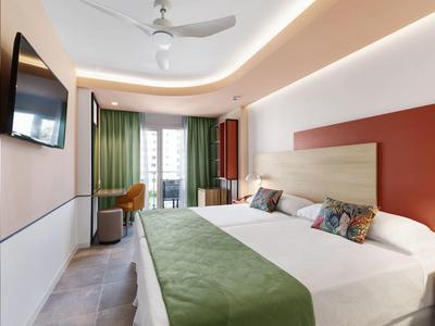 Modernes Hotelzimmer mit großem Bett, grünem Bettläufer, TV, grünem Vorhang und Balkon.