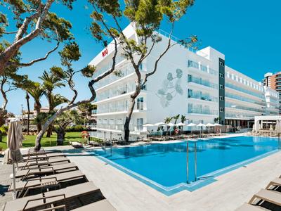 Modernes Hotel mit weißer Fassade und großem Pool, umgeben von Palmen unter klarem blauem Himmel.