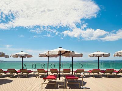 Pláž s lehátky a slunečníky před modrým mořem a zataženou oblohou.