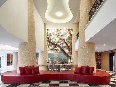 Elegantní hotelová hala s zaoblenou červenou pohovkou, kulatými sloupy a abstraktním stropním osvětlením.