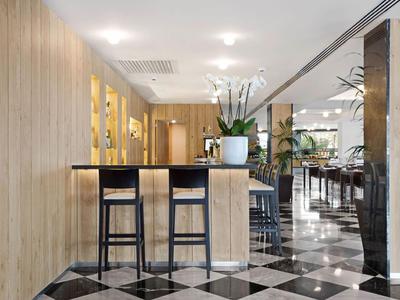 Moderní hotelový bar s vysokými židlemi a černobílou šachovnicovou podlahou.