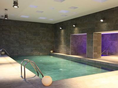 Moderní vnitřní bazén s betonovými stěnami, podvodním osvětlením a odpočinkovou zónou.