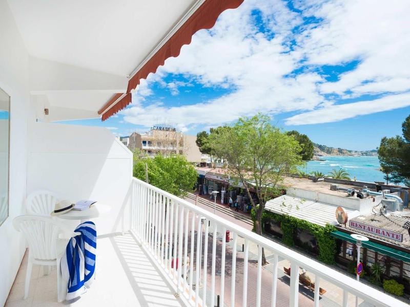 Balcon avec vue sur la mer, des arbres et un ciel bleu avec des nuages.