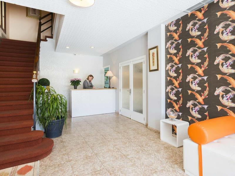 Hall lumineux avec comptoir blanc, papier peint à motif d'oiseaux colorés et sièges.