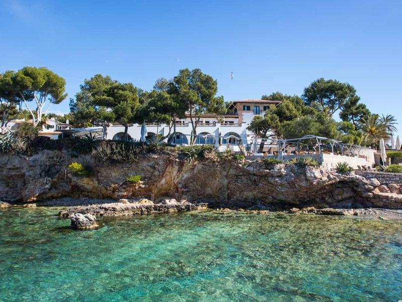 Klarer blauer Himmel, türkisfarbenes Meer, felsige Küste mit weißen Häusern und grünen Bäumen.