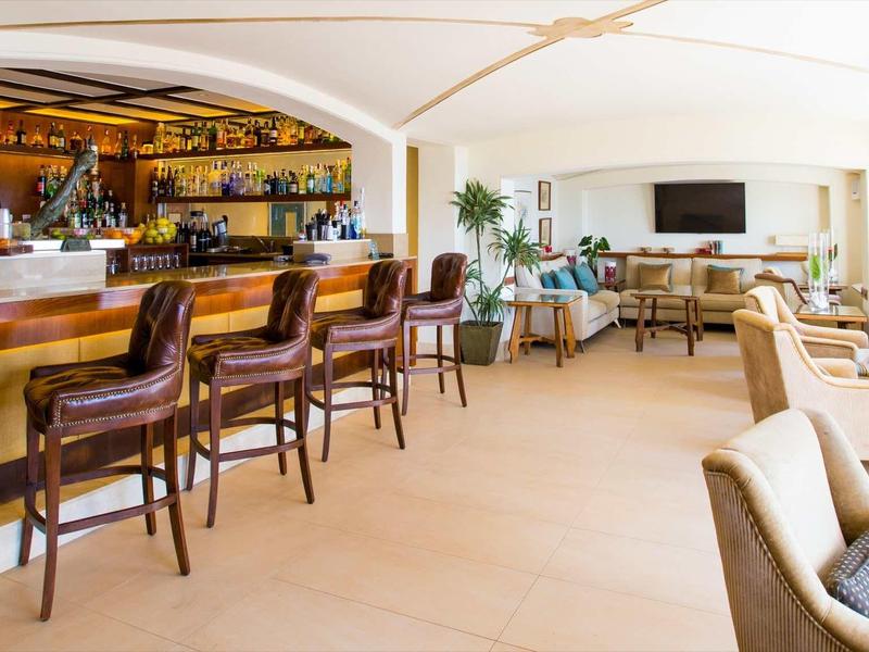 Moderner Hotelbarbereich mit Holzhockern, hellen Fliesen und gemütlichen Sitzgruppen am Fenster.