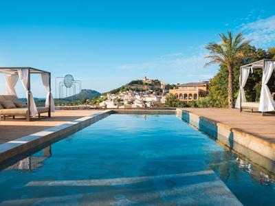 Schwimmbecken mit Liegebetten und Blick auf Palmen und Häuser unter blauem Himmel.
