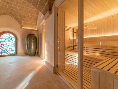 Vista interna di una sauna con panche in legno e una finestra decorativa in vetro colorato in una stanza luminosa.