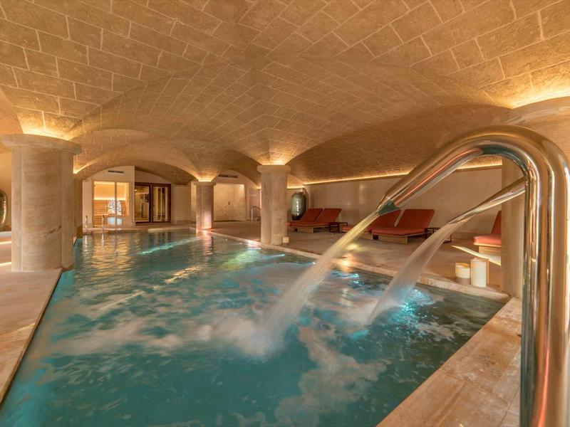 Basen kryty z wodospadem i wygodnymi fotelami w eleganckiej strefie spa.