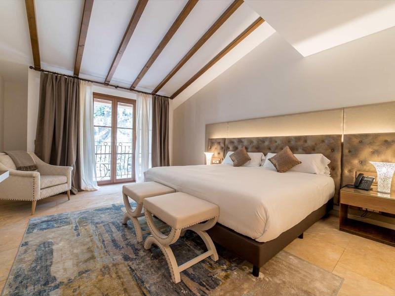 Jasno urządzona sypialnia z dużym łóżkiem, krzesłami i dywanem przy oknie z zasłonami.